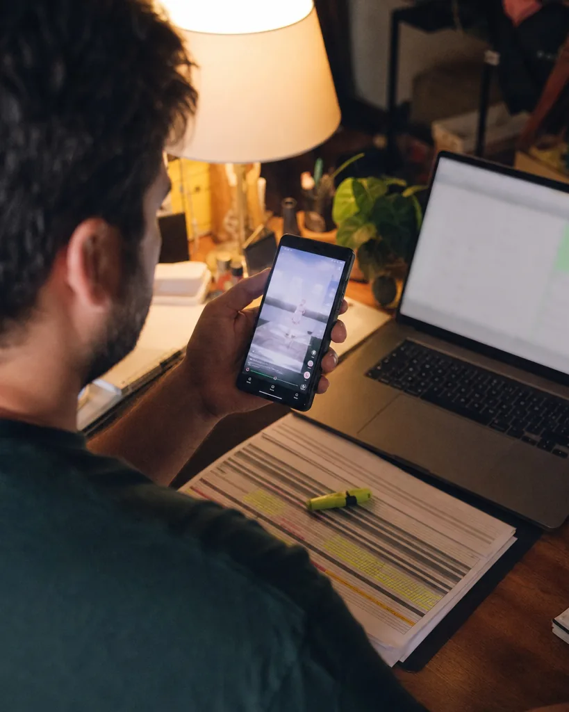 Media buyer reviewing a vertical video ad on a phone with printed results on the desk